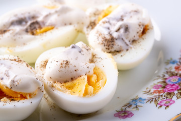 Sliced boiled eggs with mayonnaise and pepper in white plate isolated close up