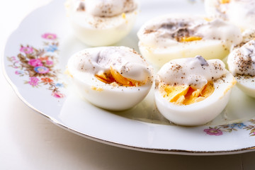 Sliced boiled eggs with mayonnaise and pepper in white plate isolated close up