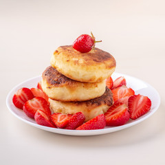Cottage cheese pancakes with sliced strawberries on white plate isolated