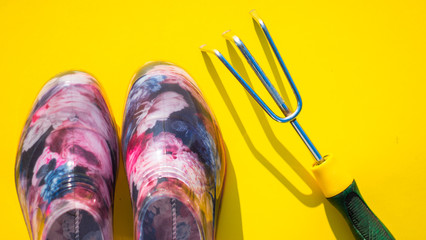 rubber boots galoshes garden fork and tool hoe on a yellow surface with copy space, top view, horizontal
