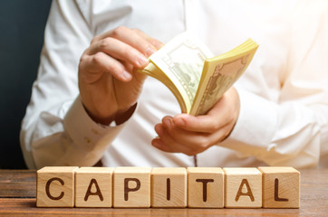 Businessman counts money on the background of the caption Capital. Capitalism, capital increase and...