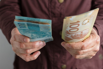 Canadian Dollars and Brazilian currency. Front view of old woman's hand handling bills.