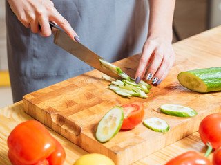 Healthy diet. Vegetarian lifestyle. Home cooking. Organic food. Closeup of female hands chopping cucumber for salad.