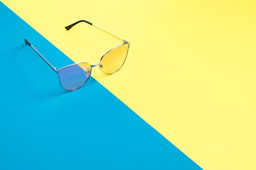 The concept of summer vacation. Top view on a sunglasses on the blue-yellow background.