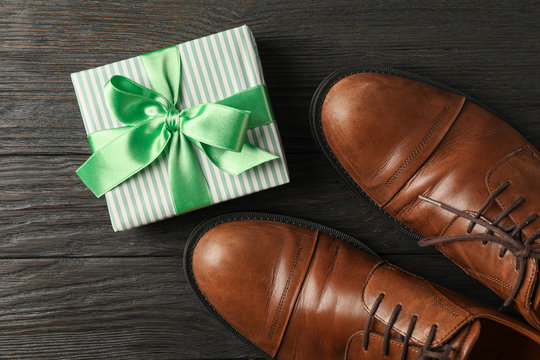 Gift box with green ribbon and brown leather shoes on wooden background, space for text and top view