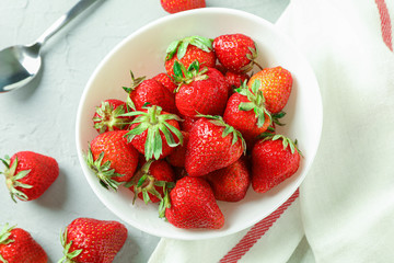 Plate with fresh strawberries, spoon and kitchen towel on white background, top view and space for text
