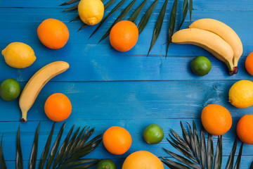 Group of exotic tropical fruits and palm leaves on blue wooden background.