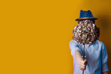 man in a hat holding a bouquet in front of his face on a bright colored background