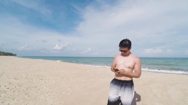 Young man taking selfies with his smartphone on the beach, summer. Man with no shirt, wearing sunglasses, taking photos at Praia de Tabatinga 2, Conde PB Brazil.