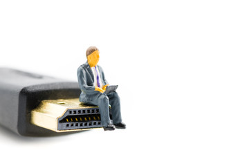 Macro shot on miniature figure as business man working on the laptop notebook sitting on HDMI plug, isolated on white background. Information technology IT and business concept