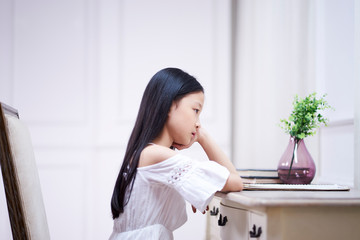 sad little asian girl sits at desk thinking