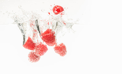 Fresh raspberries falling in water on white background