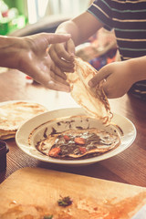 A little boy with his mother preparing together a breakfast. Mother and son smearing chocolate cream to thin pancakes. Free space