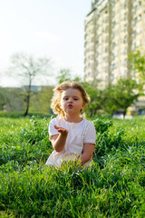 Cute little girl sending a kiss, sitting in the grass, on a sunny spring day