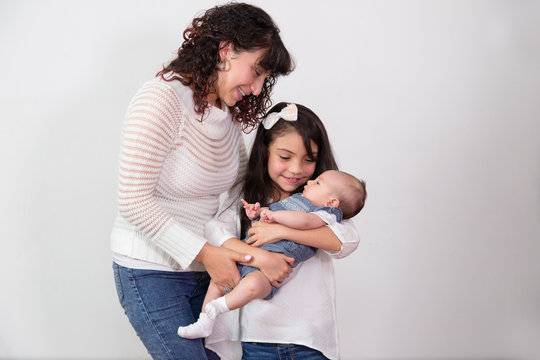 7 year old girl with her little sister in her arms smiling while her mother helps hold her with love - latin family 