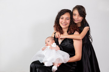 Beautiful mom sitting with her baby in her arms and her eldest daughter hugging her from behind...