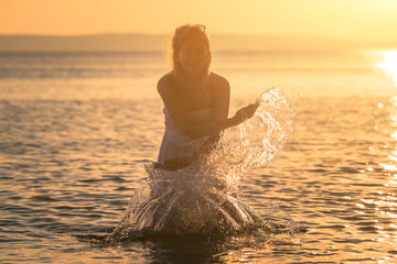 Beautiful young pregnant woman playing with water at the sea in the summer at sunset. Concept Love and pregnancy