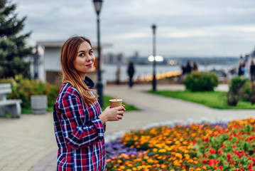 Fototapeta premium Beautiful young woman holding coffee cup and smiling in the park