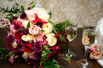 Bouquet of flowers on sweet table at wedding party. Glasses of champagne for the couple toast.