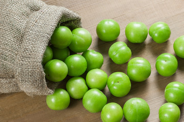 Fresh ripe organic green plums or greengage in burlap sack on wooden background, heap of may and june fruit, summer fruits concept