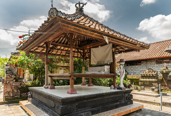 Fototapeta premium Dusun Ambengan, Bali, Indonesia - February 25, 2019: Clan compound. Open air bed under red roof in garden with memorials under blue sky. Green vegetation.