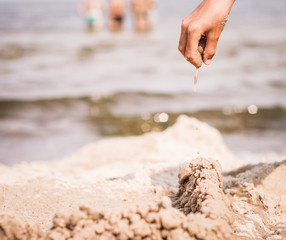 Kinderhand tropft eine Kleckerburg am Strand