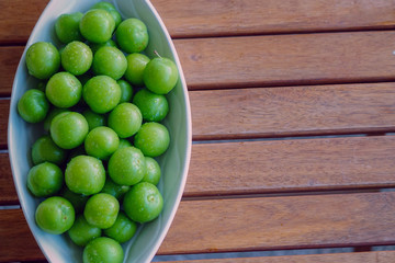 Green plums in white dish on wooden background close up view with copyspace