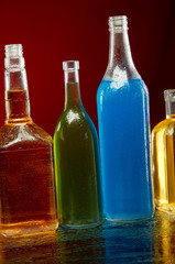 Alcohol bottles in water drops on red background