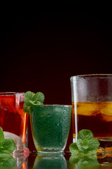 Three different alcoholic drinks in clear glasses with ice and mint on red background