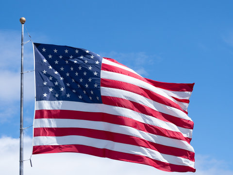 Horizontal Unfurled American Flag Against Blue Sky with Clouds