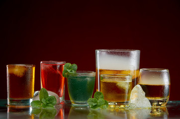 Different alcoholic cocktails with ice and mint with light smoke on a red background