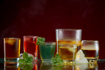 Different alcoholic cocktails with ice and mint with light smoke on a red background