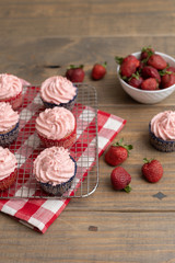 Homemade Strawberry Cupcakes on Wire Rack; One Isolated on Wooden Table; Bowl of Fresh Strawberries and Some Scattered on Table