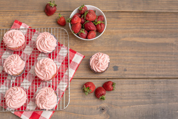 Homemade Strawberry Cupcakes on Wire Rack; One Isolated on Wooden Table; Bowl of Fresh Strawberries and Some Scattered on Table