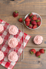 Homemade Strawberry Cupcakes on Wire Rack; One Isolated on Wooden Table; Bowl of Fresh Strawberries and Some Scattered on Table