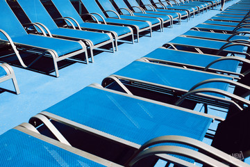 Blue lounge chairs on wooden floor on a Mediterranean sea cruise.