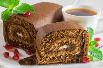 Chocolate biscuit roll and a cup of tea on white wooden table.