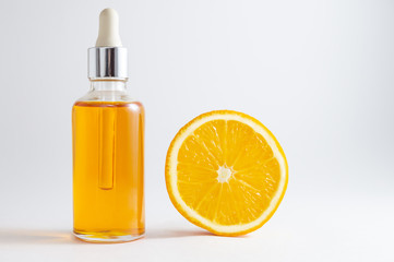 Vitamin C serum in cosmetic bottle with dropper and slice of orange on white background. Organic SPA cosmetics with herbal ingredients.