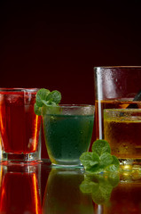 A wonderful set of alcoholic drinks in glasses with ice and mint on a red background