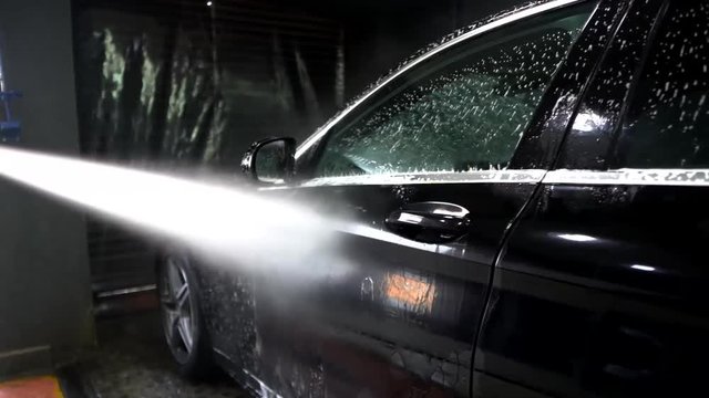 Cleaning a luxury black car after shampoo through a high pressure water nozle.
