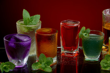 Glasses with various alcoholic drinks with ice and mint on red background