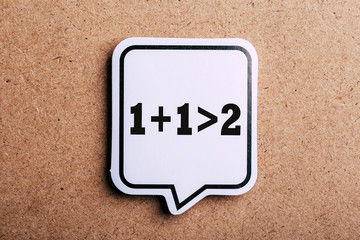 Synergy 1+1>2 Speech Bubble Isolated On Brown paper Background