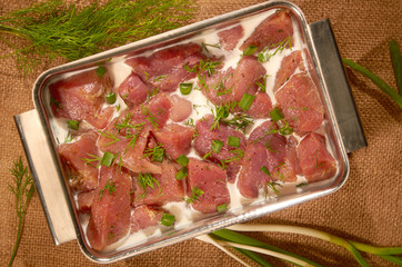 Marinated in milk and herbs, the meat in a steel pot on the cloth with fresh herbs