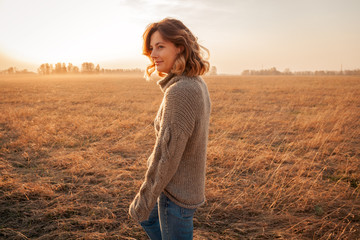 peaceful mood, eco-friendly life.Young woman with a short haircut and in stylish clothes (knitted sweater and jeans) walks and enjoys nature in the field on a summer morning