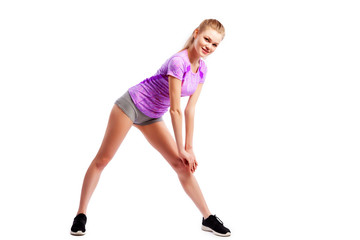 Fototapeta na wymiar A young woman in comfortable sportswear (shorts and top) is smiling charmingly and doing wide lunges to the sides with her legs on an isolated white background.