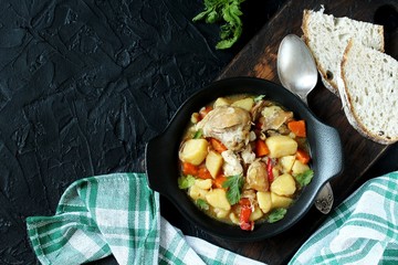 Chicken stew with potatoes and vegetables. in a black pan for serving dishes on a dark background surrounded by spices. meat and vegetables are pre-fried and then stewed. top view. copy space. 