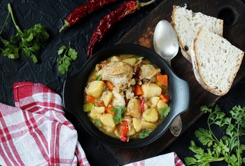 Chicken stew with potatoes and vegetables. in a black pan for serving dishes on a dark background surrounded by spices. meat and vegetables are pre-fried and then stewed. top view