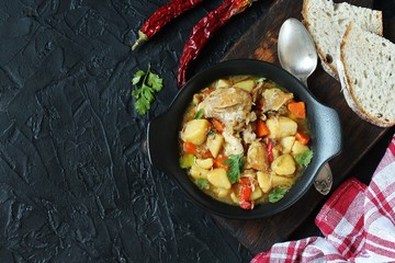 Chicken stew with potatoes and vegetables. in a black pan for serving dishes on a dark background surrounded by spices. meat and vegetables are pre-fried and then stewed. top view. copy space. 