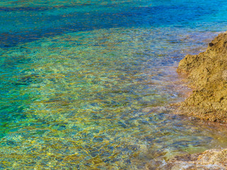 Beautiful azure blue clear water and a yellow rocky shore