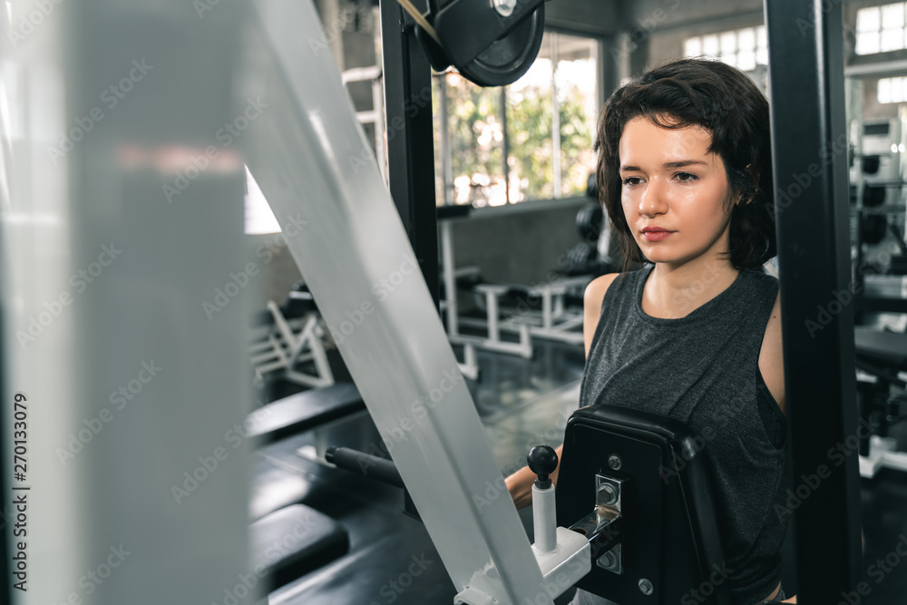 Wall mural young fitness woman execute exercise with exercise-machine in gym.